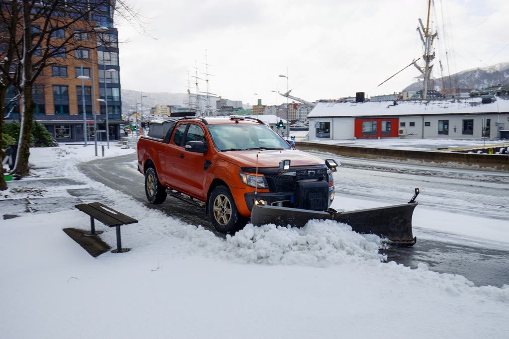 An orange pickup with a plow blade clearing a snowy road